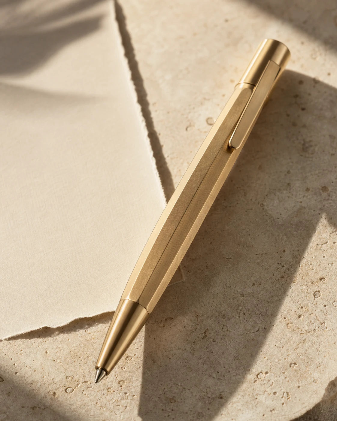 Faceted solid brass rollerball desk pen on warm limestone