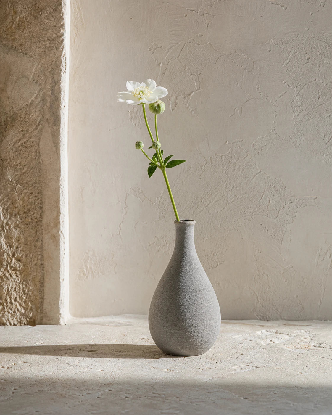 Stone-grey narrow-necked ceramic bud vase with one white stem