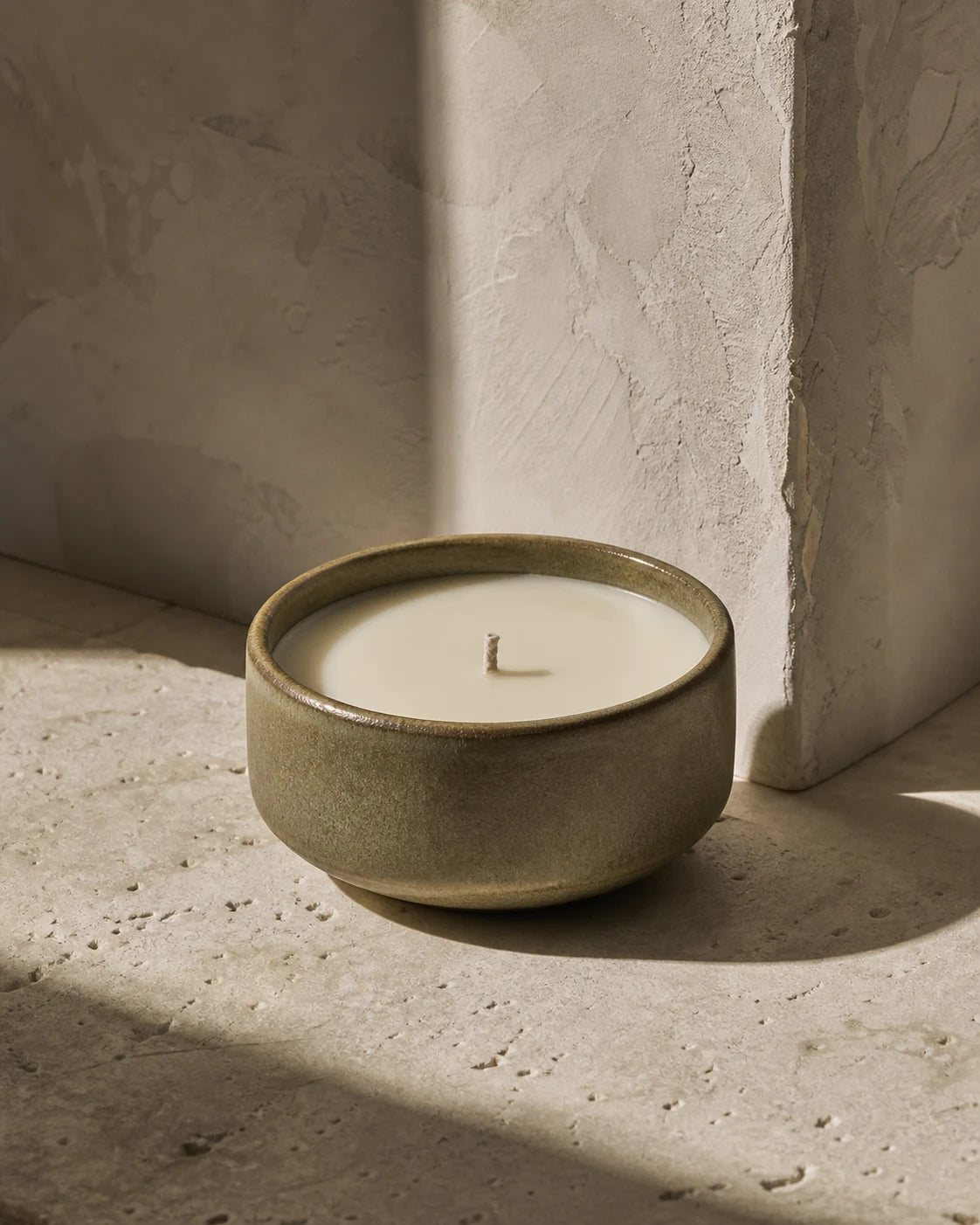 A stoneware candle glowing in warm afternoon light
